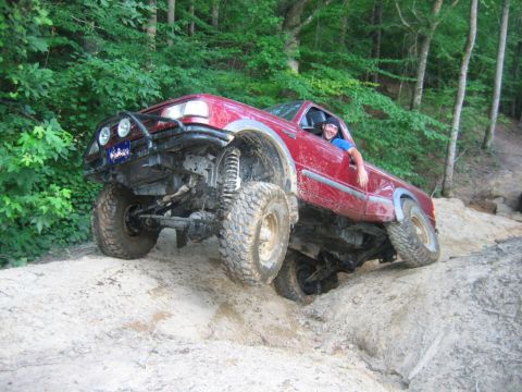 1992 Ford Mustang - A red pickup truck is shown off-roading on a dirt path with large tires and a modified bumper.