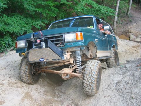1992 Ford Mustang - Modified Ford Bronco navigating rough terrain on a wooded trail.