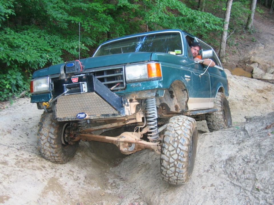 Green Ford Bronco with aftermarket bumper and winch off-roading on a dirt trail