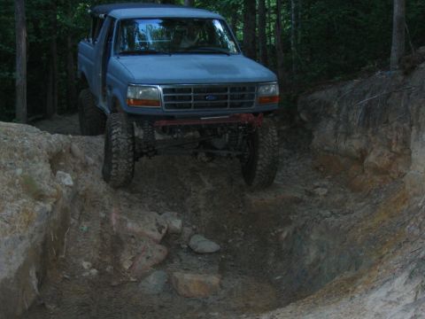 1992 Ford Mustang - A lifted Ford Bronco drives on a challenging dirt path surrounded by trees.