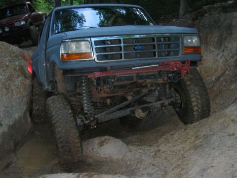 1992 Ford Mustang - A blue 1992 Ford Bronco navigates a muddy, rocky trail, with another vehicle visible in the background.