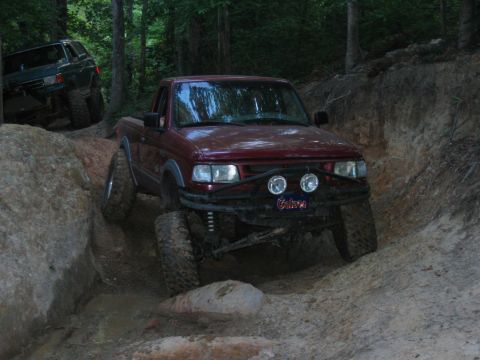 1992 Ford Mustang - Modified red pickup truck tackling a challenging off-road course with another vehicle behind.