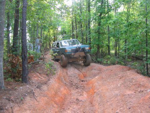 1992 Ford Mustang - A green SUV navigates a challenging off-road trail through a wooded area.