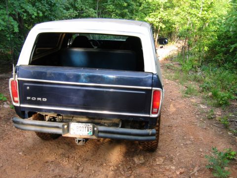 1992 Ford Mustang - Rear view of a dark blue Ford Bronco with a white top, parked on a dirt road.