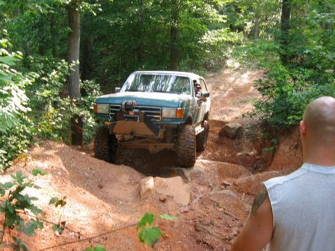 1992 Ford Mustang - Teal Ford Bronco navigating a challenging off-road trail through a wooded area.