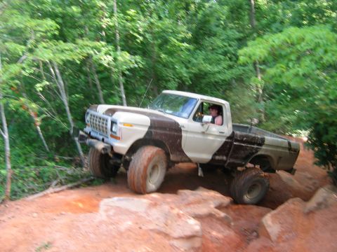 1992 Ford Mustang - A lifted Ford pickup truck navigates a rocky off-road trail surrounded by trees.