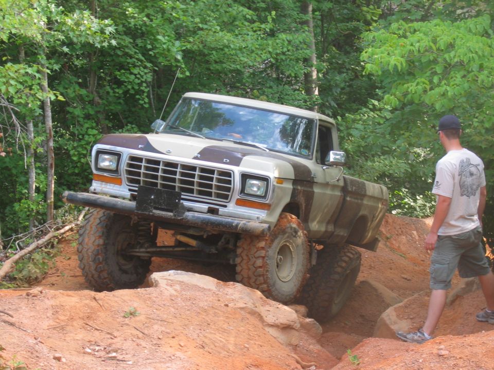 Camouflaged Ford F-Series pickup truck with lifted suspension and off-road tires navigating a rocky incline