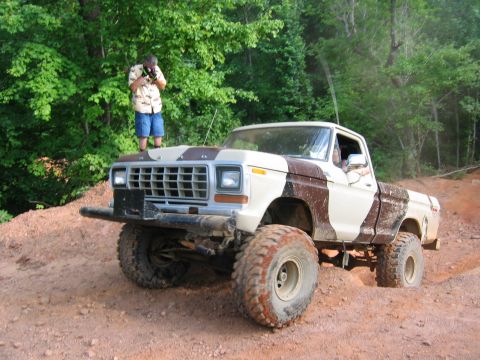 1992 Ford Mustang - A lifted Ford F-Series pickup truck with a camouflage paint scheme navigates a dirt path while a person stands on its hood.