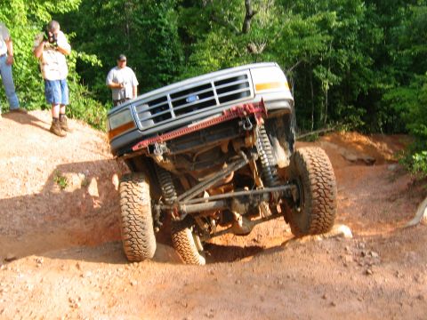 1992 Ford Mustang - A lifted silver Ford Bronco navigates a steep, muddy incline during an off-road excursion.