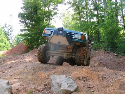 1992 Ford Mustang - A modified green truck navigates a challenging off-road course with steep inclines and loose dirt.