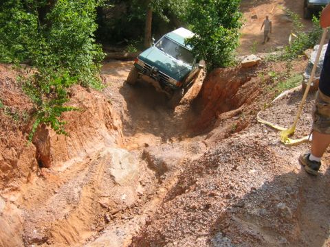 1992 Ford Mustang - An off-road vehicle navigates a challenging dirt path, with another vehicle and a person visible in the distance.