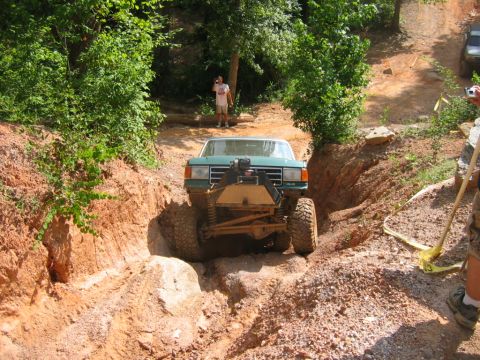 1992 Ford Mustang - A modified truck navigates a challenging off-road trail, with another vehicle visible in the background.