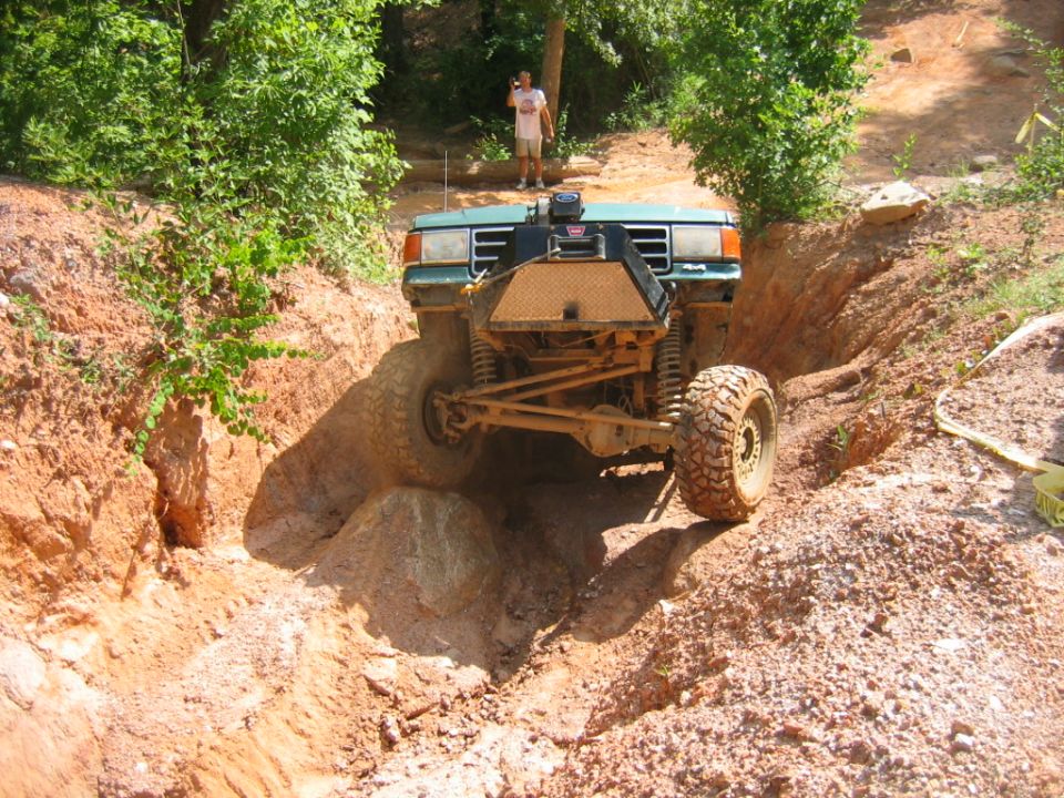 Green off-road vehicle with large tires navigating a dirt trench, front view