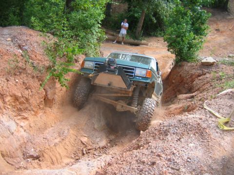 1992 Ford Mustang - This modified pickup truck navigates a challenging off-road trail, demonstrating its suspension and tire capabilities.