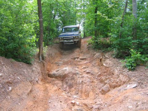 1992 Ford Mustang - A blue 1970s Ford F-Series truck tackles a challenging rocky trail in a wooded area.
