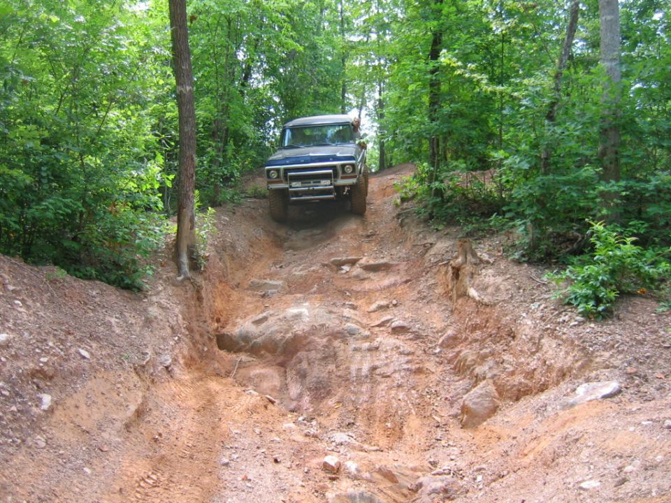 Blue 1970s Ford F-Series truck navigating a steep, rocky off-road trail