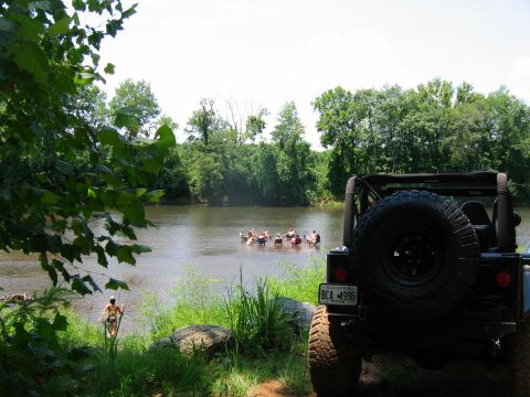 1992 Ford Mustang - A group enjoys a sunny day tubing down a river, with a Jeep parked nearby.