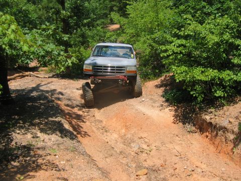 1992 Ford Mustang - A lifted pickup truck navigates a steep dirt trail surrounded by dense green foliage.