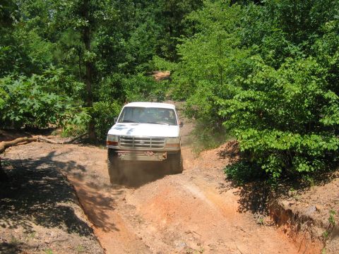 1992 Ford Mustang - A white Ford F-150 truck navigates an off-road trail, kicking up dust as it ascends a dirt incline.