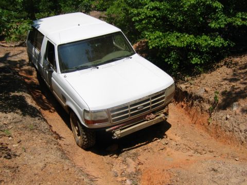1992 Ford Mustang - A white SUV navigates a steep dirt trail surrounded by lush green foliage.