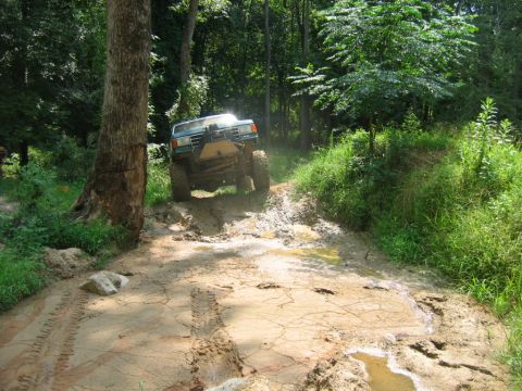 1992 Ford Mustang - A modified truck navigates a challenging muddy off-road path through a forest.