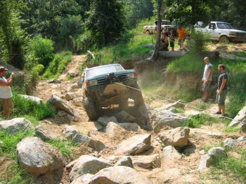 1992 Ford Mustang - A green off-road vehicle is being winched over a rocky obstacle, with spectators gathered nearby.
