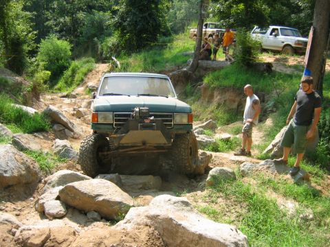1992 Ford Mustang - A green off-road truck navigates a challenging rocky course with spectators watching.
