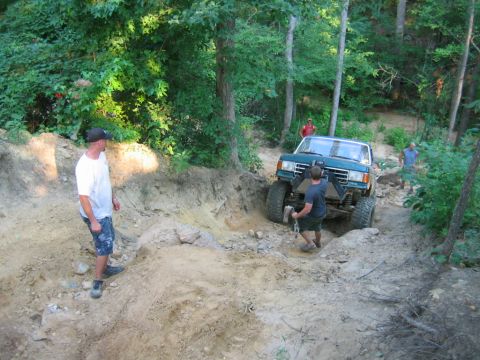 1992 Ford Mustang - A teal pickup truck is being winched up a challenging off-road trail with several people observing the vicinity.