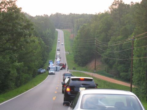 1992 Ford Mustang - A long line of cars and emergency vehicles are stopped on a two-lane road due to an overturned vehicle.