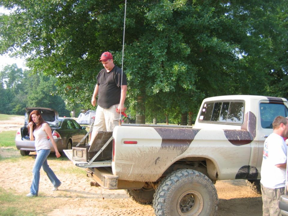 Muddy pickup truck with camouflage pattern on bed, people around