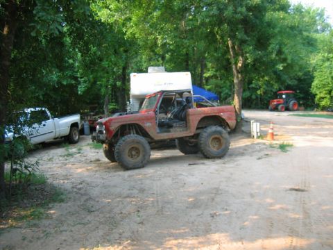 1992 Ford Mustang - A modified red SUV with oversized tires sits in a sandy area next to a white pickup truck and a camper.