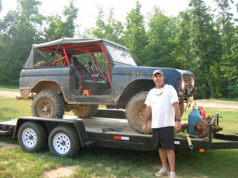 1992 Ford Mustang - A man stands beside a dark-colored Ford Bronco loaded onto a trailer.