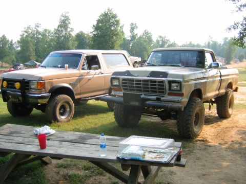 1992 Ford Mustang - Two lifted Ford trucks, a Bronco and a pickup, are parked together on a grassy area with trees in the background.