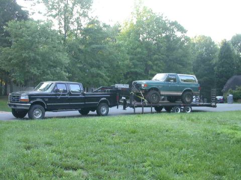 1990 Ford Bronco - A black Ford F-250 pickup truck tows a green Ford Bronco on a flatbed trailer.