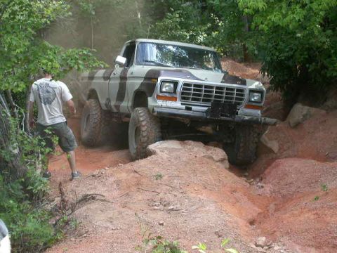 1990 Ford Bronco - A Ford F-Series truck navigates a challenging off-road trail with a person observing.