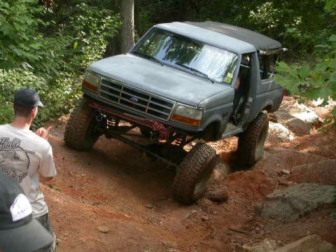 1990 Ford Bronco - This Ford Bronco is navigating a steep, rocky, off-road trail with a person observing its progress.