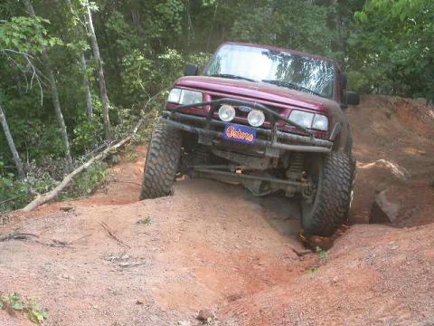 1990 Ford Bronco - This red SUV is navigating a steep, sandy incline on a wooded trail.