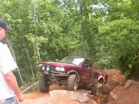 1990 Ford Bronco - A red truck navigates a challenging rocky trail, with a person watching from the left.
