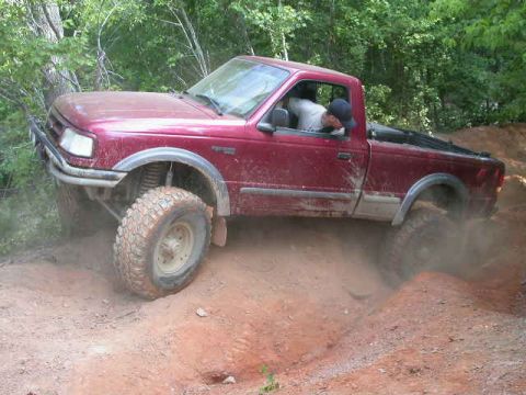 1990 Ford Bronco - A red pickup truck navigates a challenging dirt path with its tires kicking up dust.