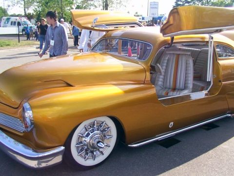 1998 Ford Taurus - A customized gold coupe with its gullwing doors open at a car show.