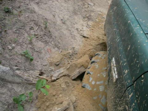 1990 Ford Bronco - A green SUV is stuck in a dirt embankment, with its tire partially buried.