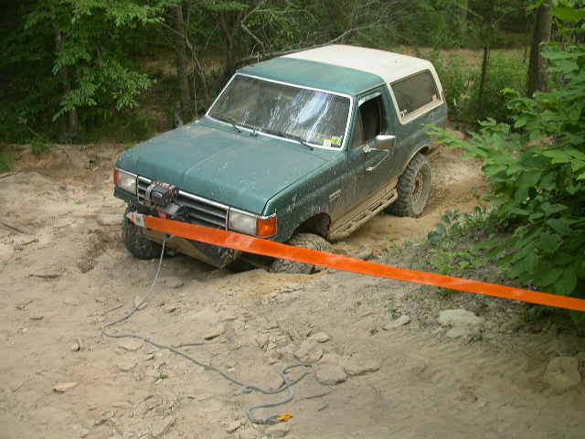 Green 1990 Ford Bronco with winch on front bumper, stuck in dirt