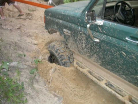 1990 Ford Bronco - A green 1990 Ford Bronco is stuck in the mud, with its front wheel sunk deep into the dirt.