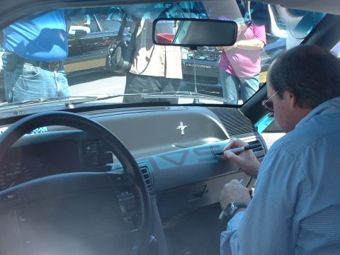 2000 Ford Crown Victoria - A man signs the dashboard of a Ford Mustang while other vehicles are seen through the windshield.