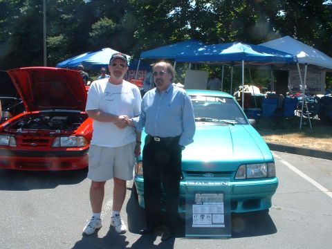 2000 Ford Crown Victoria - Two men pose with a teal Saleen Mustang and a red Ford Mustang at an outdoor car show.