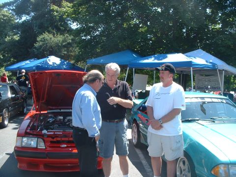 2000 Ford Crown Victoria - Three men converse near a red Ford Mustang and a teal car at an outdoor event.