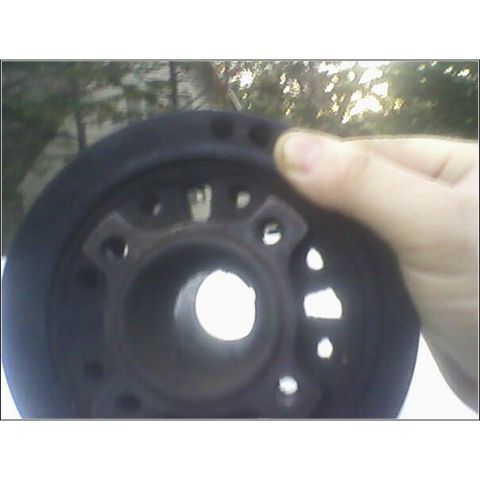 1972 Ford Ranchero - A hand holds a black pulley, revealing its mounting holes and outer circumference against a blurred outdoor background.