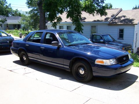 2002 Ford Crown Victoria - A blue 2002 Ford Crown Victoria is parked in front of a house with a pickup truck behind it.
