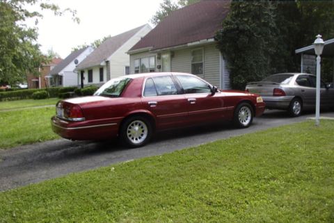 1999 Ford Crown Victoria - Maroon sedan parked on a driveway with another car behind it.