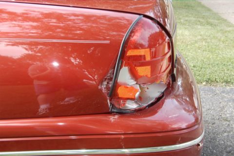 1999 Ford Crown Victoria - The rear passenger side of a red car shows a cracked and broken taillight assembly, with visible damage to the fender.